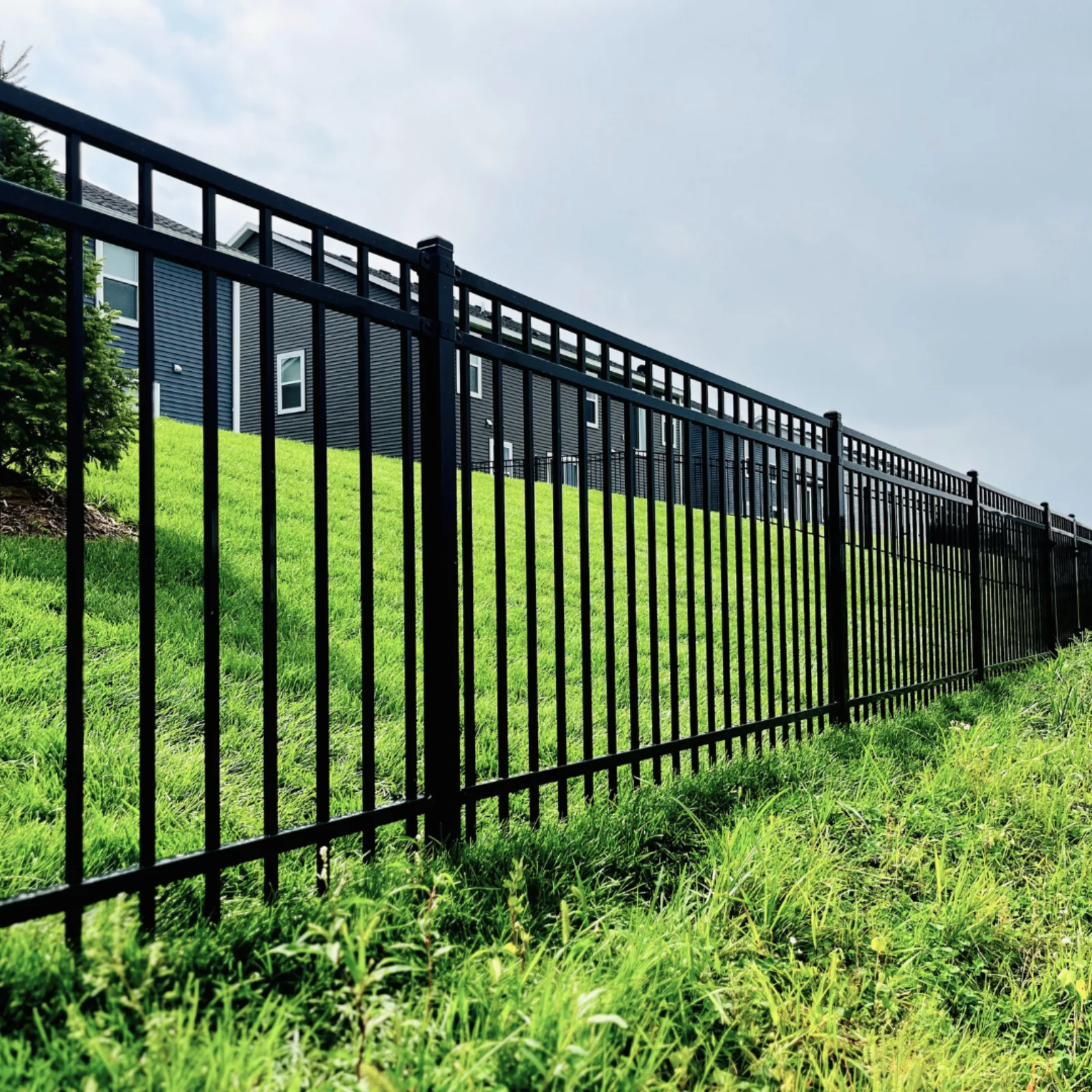 Black ornamental steel fence installed on a green hillside in the Minneapolis metro